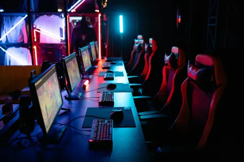 Stock photo of several gaming PCs in a line with racer chairs in a dark room with LED lighting